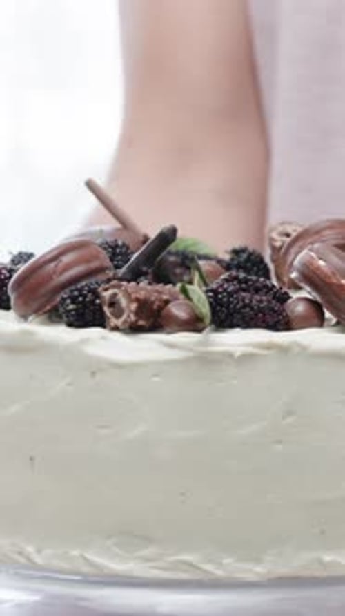 Vertikales Video. Eine Frau dreht ihren fertigen Kuchen mit schönen Schokoladendekorationen darauf