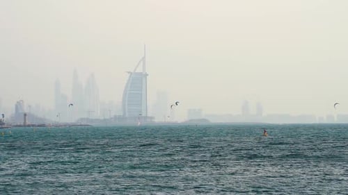 Steady shot of kite surfers next to the Burj Al Arab hotel and the Dubai Skyline at the background a