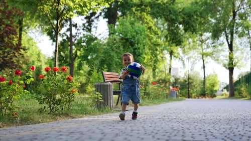 Happy smiling child with a ball running in the park. Active baby boy throws the ball on the road.