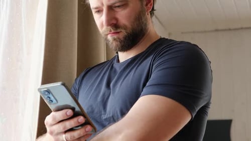 Bearded Man Scrolling on Cell Phone Indoors