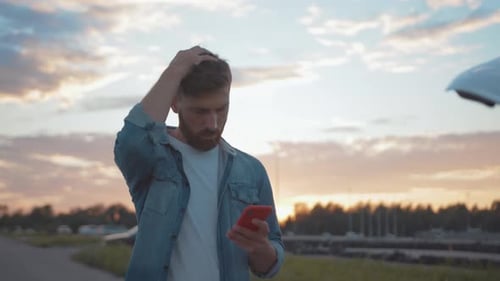 Man Uses Phone with Broken Down Car at Sunset