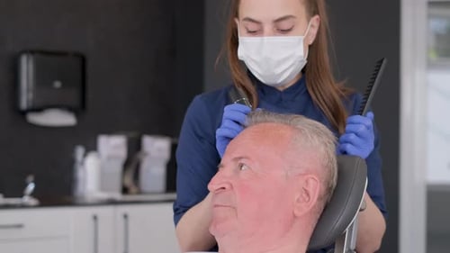 Medical Professional Examines Older Man's Hair in Clinic