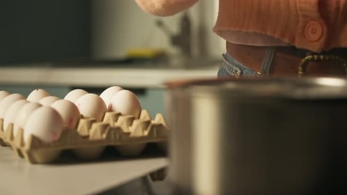 Person, die frische Eier mit einem Löffel in einen Topf mit kochendem Wasser in der Küche legt - Ostereier