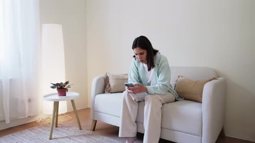 Woman on Sofa Looking at Mobile Phone