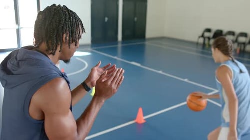 Coaching basketball practice, trainer clapping while female players dribbling in gym