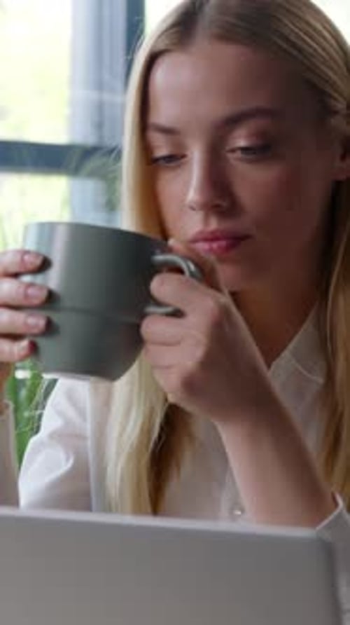 Woman drinking coffee while looking at laptop