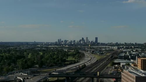Aerial drone panning shot over the train tracks and highway with the high skyline of Denver in the b