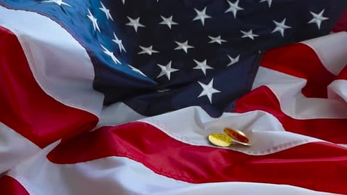 Goldene Bitcoin-Kryptomünzen fallen in Zeitlupe auf eine amerikanische US-Flagge und drehen sich langsam.
