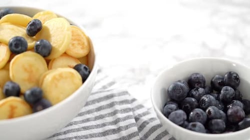 Step By Step Freshly Made Mini Pancake Cereal with Fresh Blueberries in a White Bowl