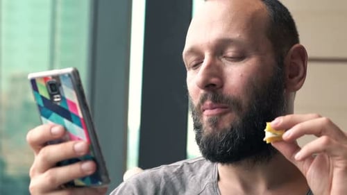 Young man enjoys sweet treat and texting on smartphone in local cafe