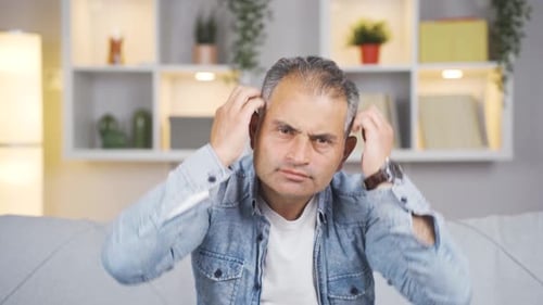 Man with Gray Hair Sitting on Couch Scratching Head