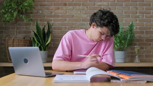 Young Male College Student Studying at Home Writing in Notebook