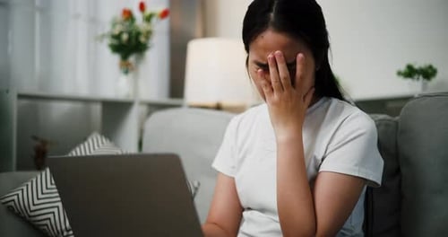 Asian woman looks distraught after receiving devastating news on laptop