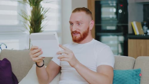 Smiling man video chatting on tablet on couch