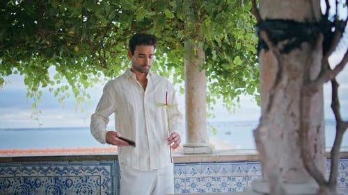 Man on Balcony Uses Phone and Holds Flower