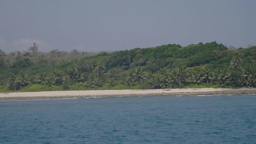 Sailing past a remote island with azure blue sea white sand and trees up to the sand edge with no ho