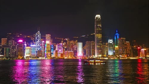 Neon illuminated Hong Kong waterfront skyline flashing along horizon as boat passes through scene ma