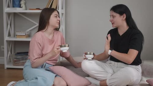 Teetrinken auf dem Boden im Wohnzimmer Zwei Mädchen unterhalten sich, lachen und halten Teetassen aus Porzellan