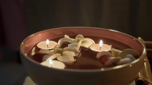Close-up of Glossy Bowl Filled with Water, Floating Candles, and White Petals