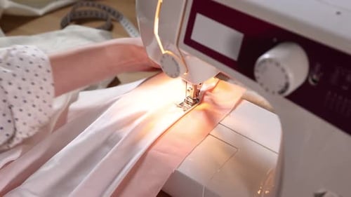 Woman sewing fabric with professional machine at wooden table in workshop, closeup