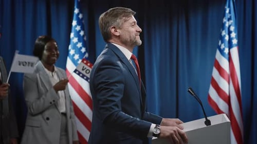 Politician Giving Speech at Press Conference With Flags
