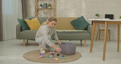 Woman cleaning up children's toys into basket indoors