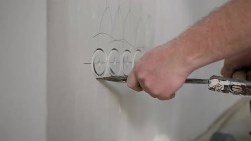 A Male Repairman Knocks Holes for Electrical Outlets in the Wall with a Hammer and Chisel