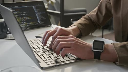 Unknown Man Typing on Laptop Keyboard Coding Software at Office Desk