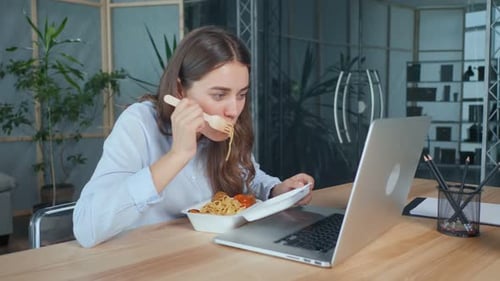 Businesswoman Having Lunch Sitting at an Office Table With a Laptop Fast Food