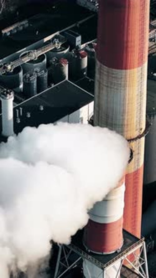 Smoke rising from industrial smokestack during daylight in city
