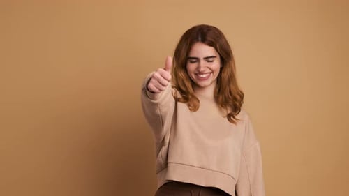 Smiling Woman Giving Thumbs Up on Tan Background