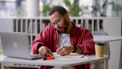 Successful University Graduate Student Talking on Phone Taking Notes Working Remotely on Laptop
