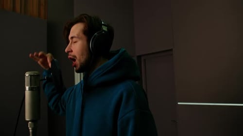 Rap singer with headphones and microphone emotionally recording new song in professional studio