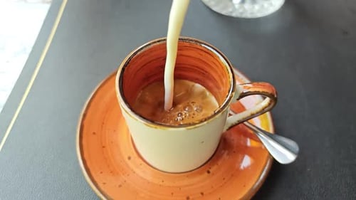 Milk being poured into coffee mug on table