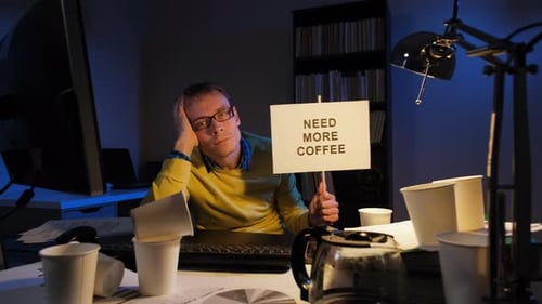 Man at Desk Holds Need More Coffee Sign