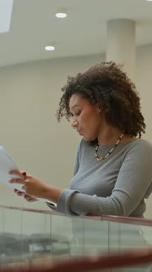 Black Female Manage Reading Document while Standing in Modern Office Center