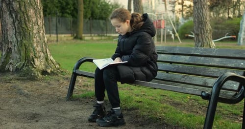 Teen Reading Book on Park Bench