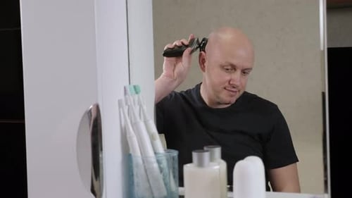 Man Shaves Head in Front of Bathroom Mirror