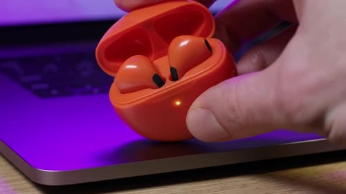 Orange Wireless Earbuds and Charging Case on Laptop