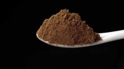 Dried nutmeg spice on a spoon is poured out isolated on a black background. Dry seasoning in spoon
