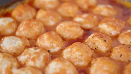 Fleischbällchen in einer Backform, die gerade aus dem Ofen kommt, mit sprudelnder und köchelnder Sauce, Nahaufnahme.