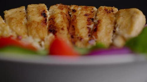 Extreme close up of a bowl of grilled vegan meat and fresh vegetables on a bed of rice, cucumber, re
