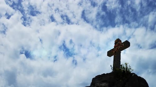 a statue of a cross over the mountains with a timelapse background of the clouds in the sky.