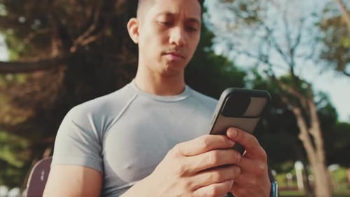 Young man sitting on a park bench uses a mobile phone