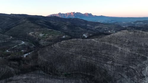 Aerial view flying over hillside forest fire natural disaster with sunrise mountain range in the dis