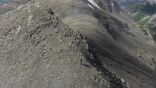 Drone shot of a man running carefully down the rocky slopes of the mountain ridge on Schilthorn, Swi