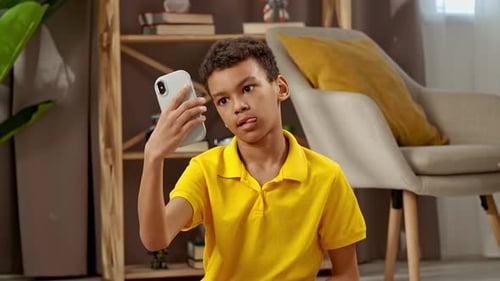 Boy Making Faces While Using Smartphone Indoors