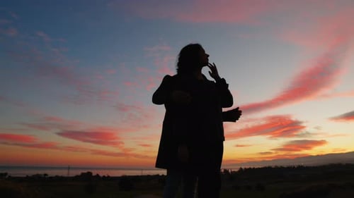 Couple Silhouetted Embracing at Pink and Orange Sunset