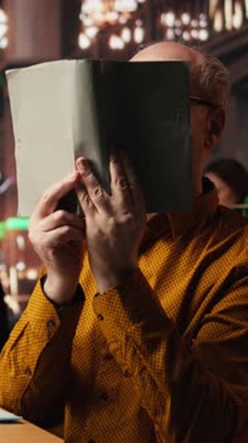 Vertical Video Wise Aged Person Reading a Book at the Public Library and Enjoying Free Time