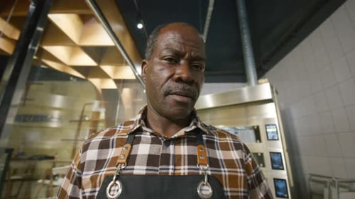 Black Bakery Worker Carrying Tray of Freshly Baked Croissants in Kitchen
